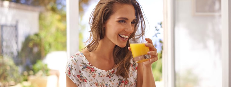 une femme boit un verre de jus d'orange riche en vitamine C