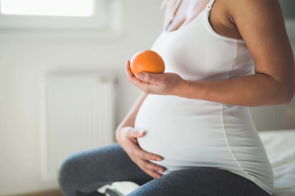 une femme enceinte tient une orange